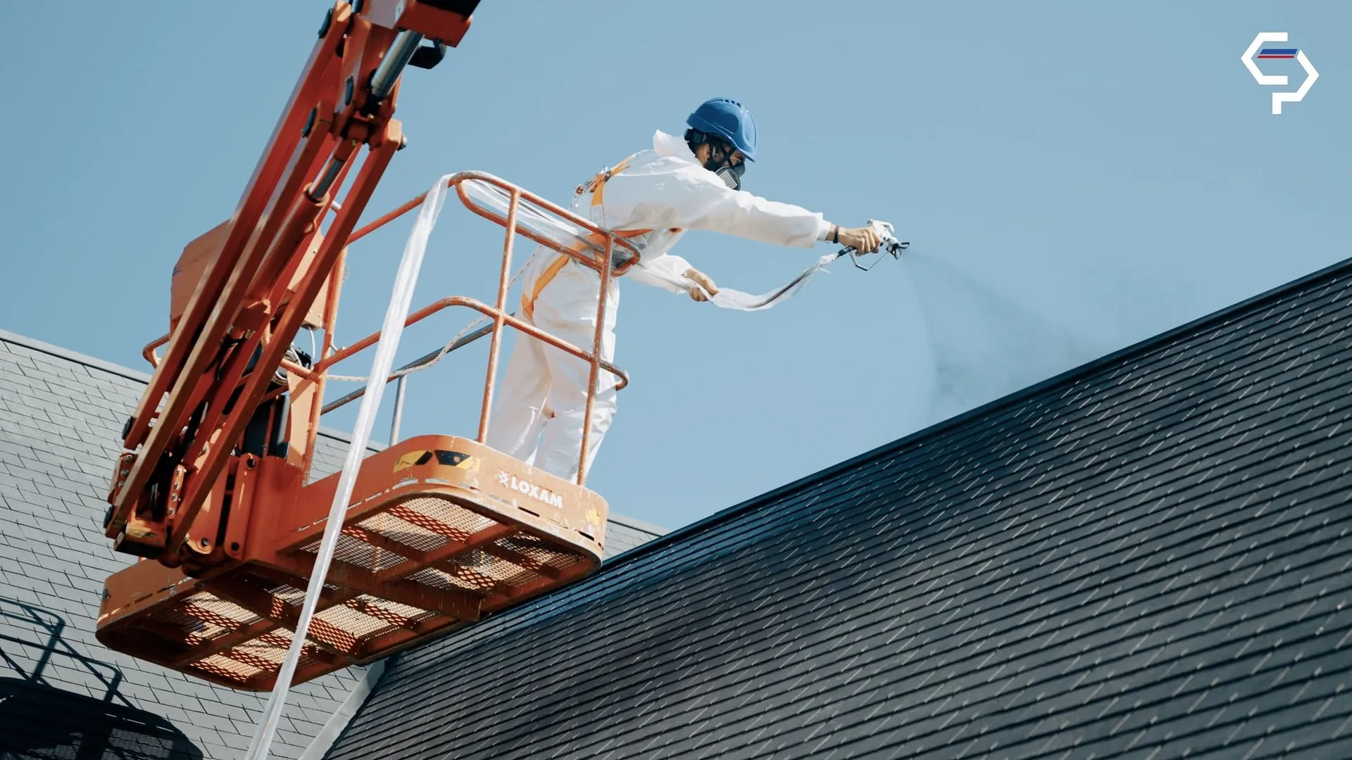 Roofer spraying a treatment onto a roof from a cherry picker on a Les Compagnons du Patrimoine site