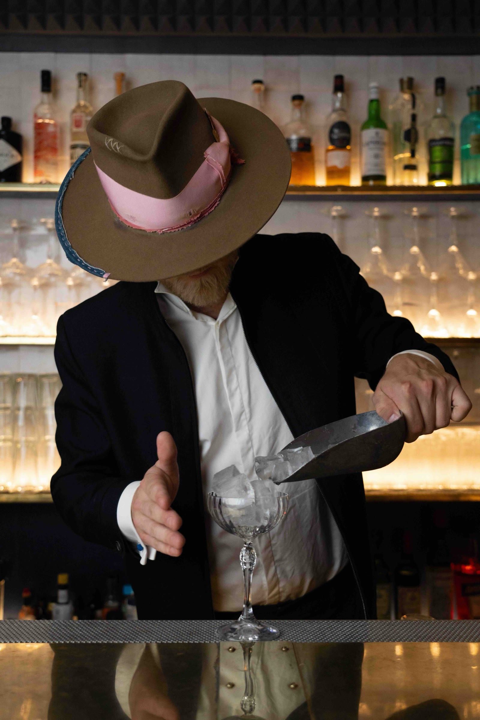 Le barman des Désinvoltes en chapeau, derrière son comptoir