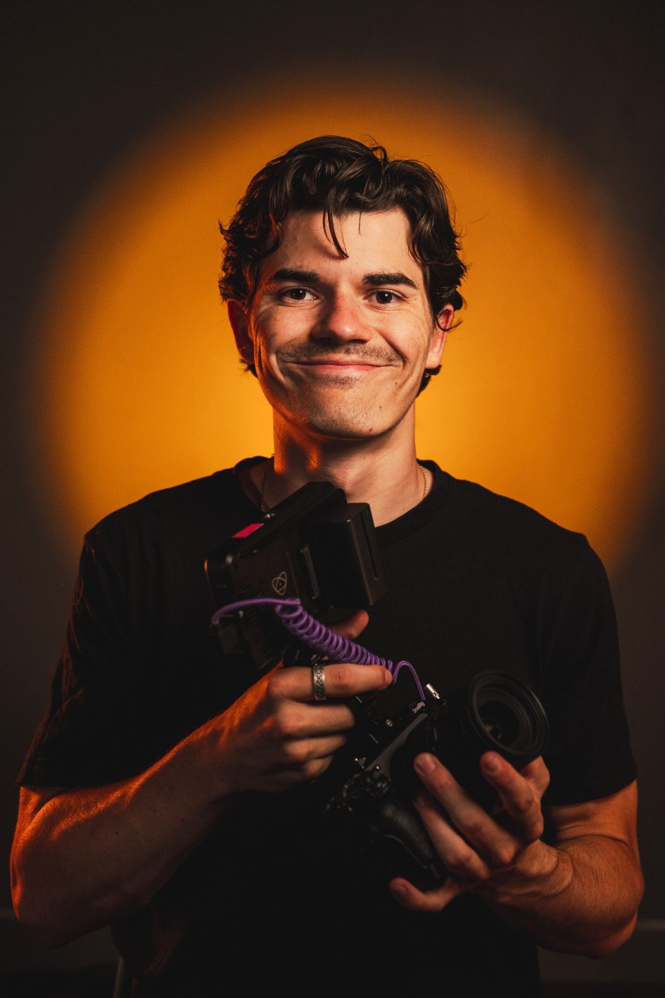Portrait de Marius Kermoal, caméra en main, devant un halo de lumière orange