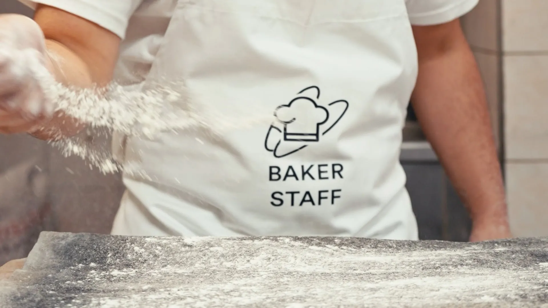 Baker at work in a Baker Staff apron, with flour in the air