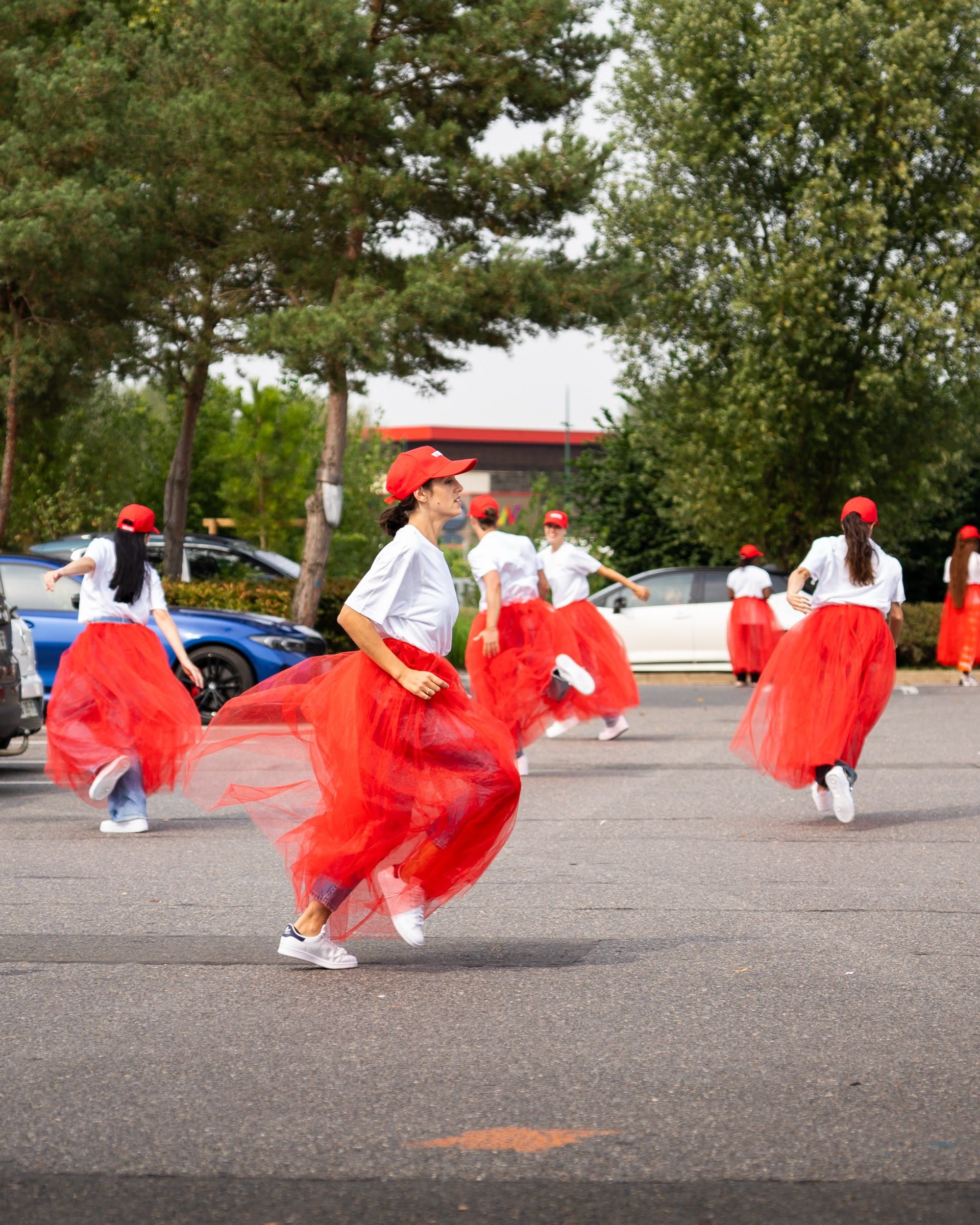 Danseuses en jupes de tulle rouge et casquettes Velux sur un parking